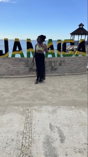 Chikumo standing in front of a Jamaica sign on a sunny trip